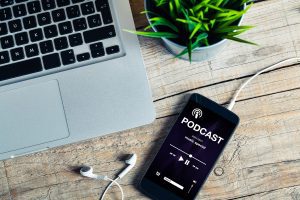 Mobile phone on wooden desk with podcast app on the screen.