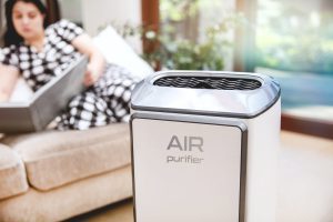 Modern air purifier cleans up the air in the living room with woman reading a book on couch in the background.